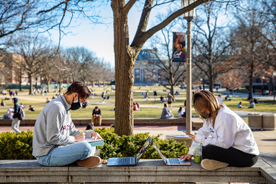 two masked students studying on the quad