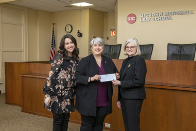 Program coordinator, dean, and trustee pose at law school with check