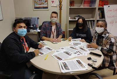 masked diverse students sitting around table with fliers