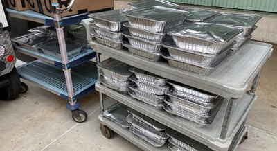 Covered foil tins of food stacked on rolling cart