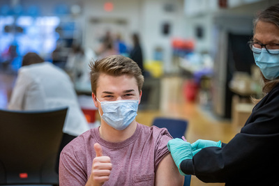 Masked student gives thumbs up as he receives the vaccine