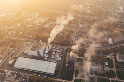 overhead view of factory in neighborhood emitting smoke from smokestacks
