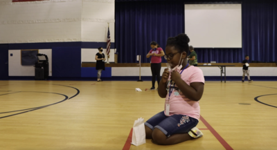 child kneeling on gym floor spitting into tube